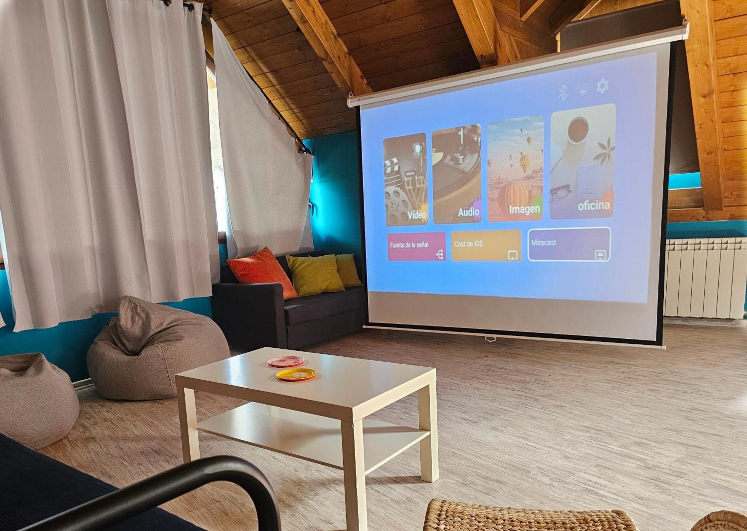 Un salón moderno con una pantalla grande mostrando una presentación, un sofá, una mesa de centro y vistas del techo de madera.