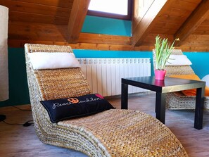 Een rieten lounge stoel met een kussen, een tafeltje met een roze plantpot, en een radiator op de achtergrond.