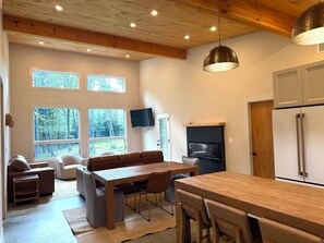 A modern kitchen with a wooden ceiling, large windows, a dining area, and a built-in oven.