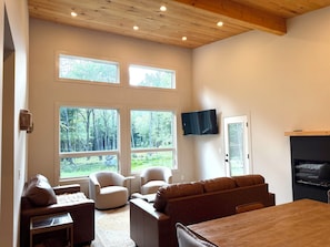 A modern living room with a wooden ceiling, large windows, a flat-screen TV, and a fireplace.