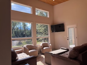 A room with large windows, a flat-screen TV, and two leather sofas.