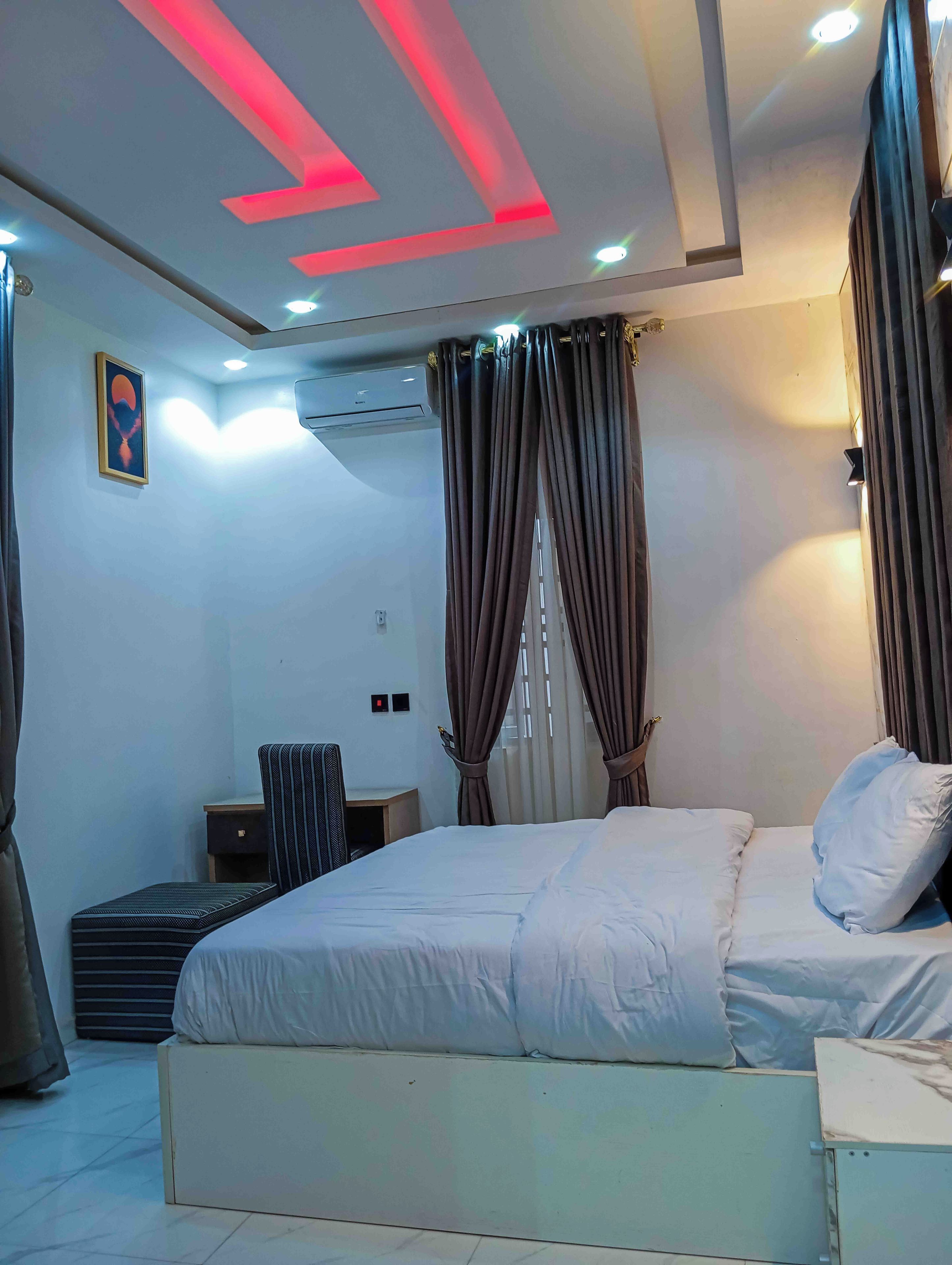 Un dormitorio moderno con cama, cortinas, aire acondicionado y un escritorio.