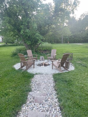 A garden with four Adirondack chairs arranged around a fire pit, surrounded by a gravel path.