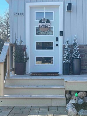 A white door with a 'Season's Greetings' sign, a mailbox, and a small Christmas tree.