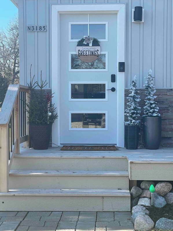A white door with a 'Season's Greetings' sign, a mailbox, and a small Christmas tree.