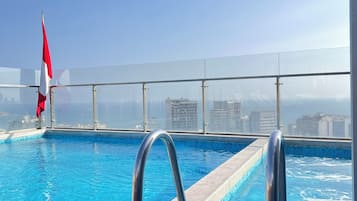 A rooftop pool with clear blue water, metal railings, and a flagpole with a flag.