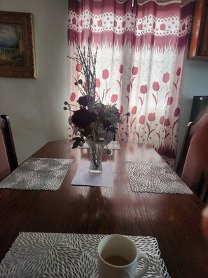 A dining table with a vase of flowers, a cup of coffee, and patterned placemats.