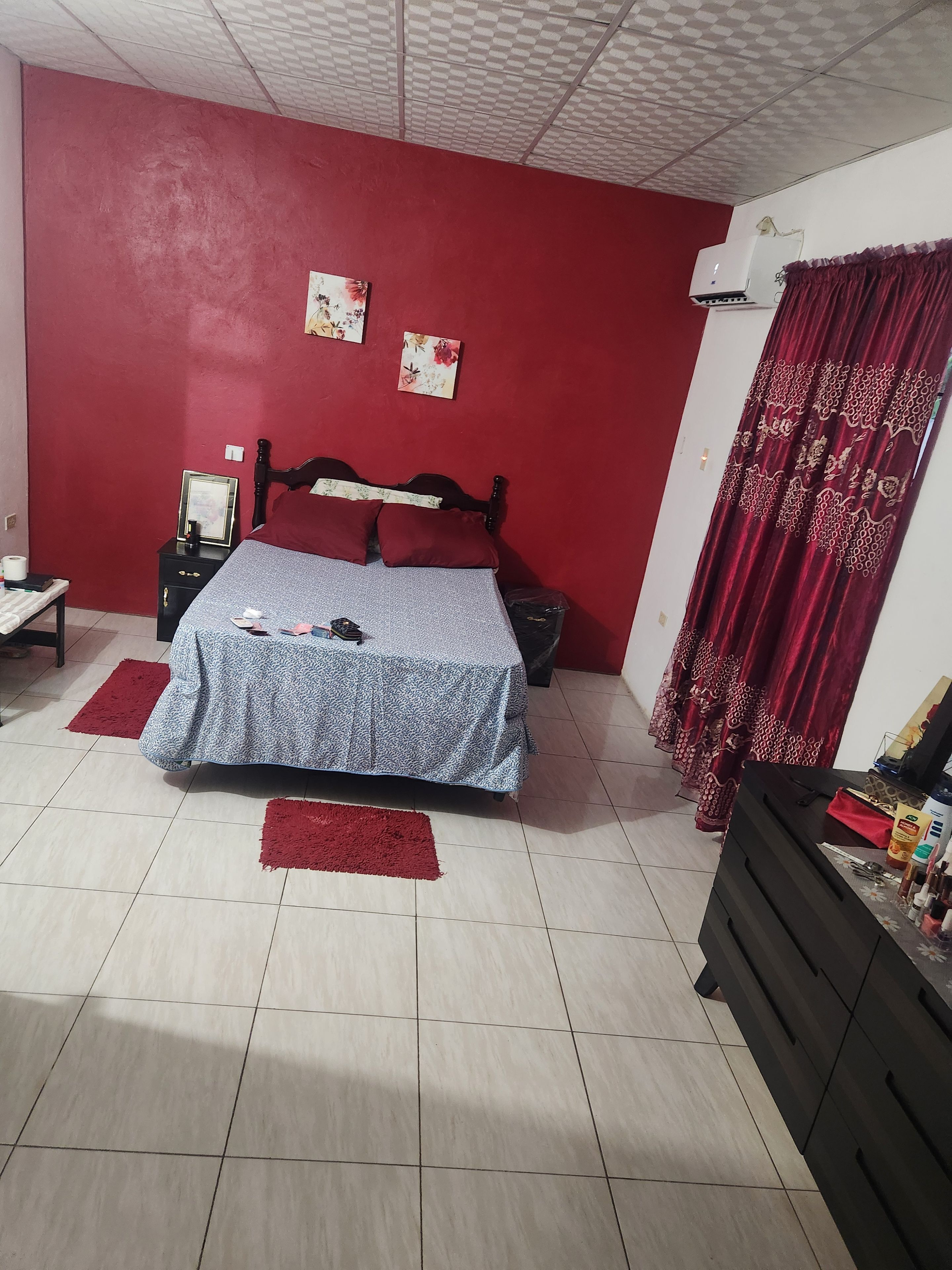 Un dormitorio con cama, mesitas de noche, cómoda y cortina roja.