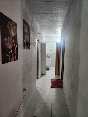 Un pasillo con piso de baldosas, una puerta que da a un baño y una pared con un cuadro floral.