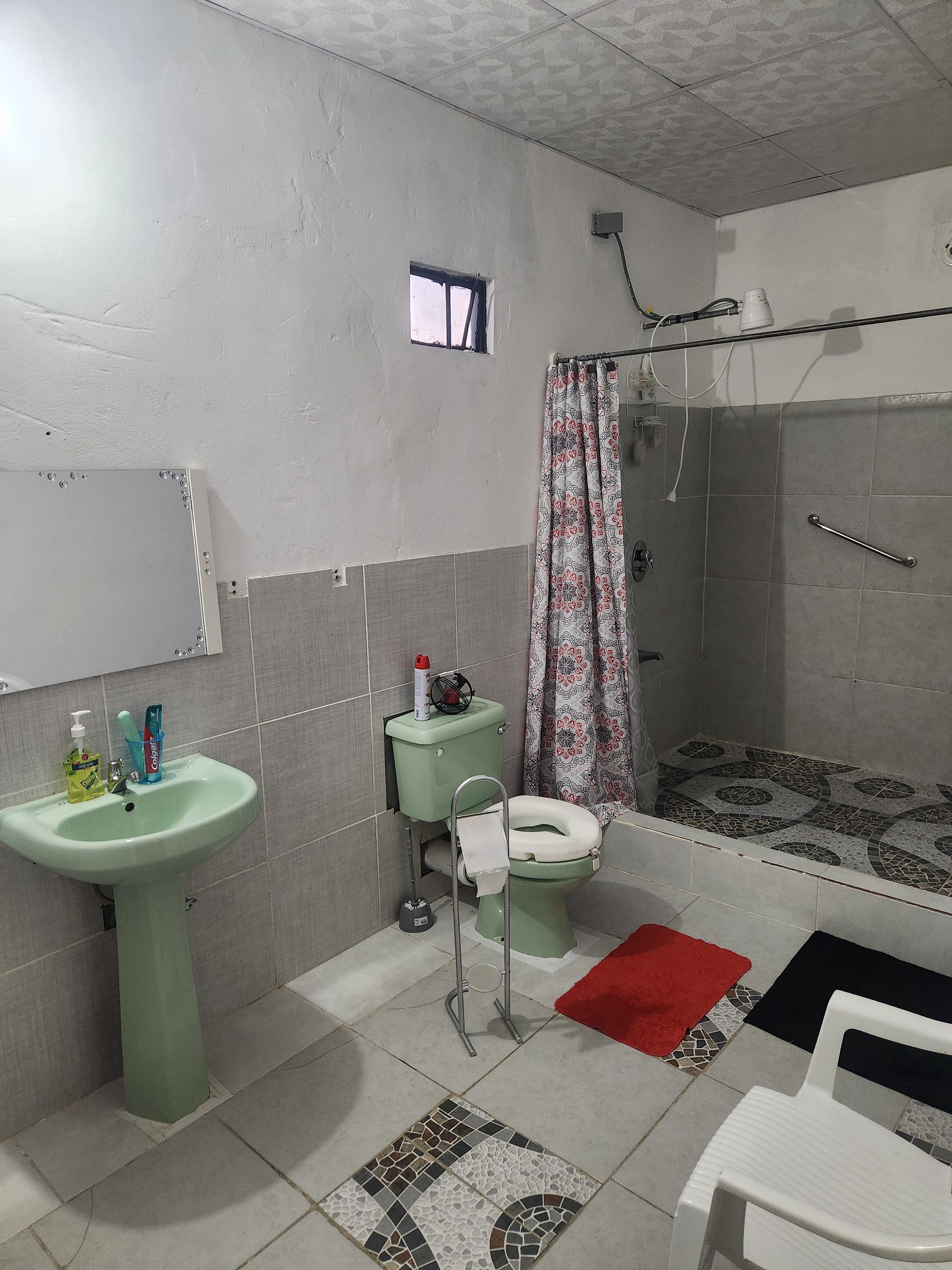 Un baño con inodoro, lavamanos, ducha y una ventana pequeña.