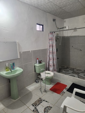 A bathroom with a toilet, sink, shower, and a small window.