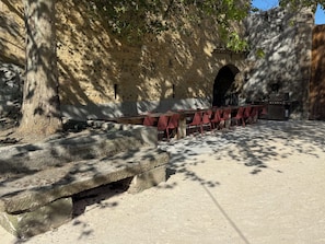 Un espacio exterior con mesas y sillas rojas, una parrilla de barbacoa y un muro de piedra.