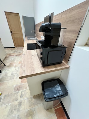 Una kitchenette con cafetera, un lavabo y un cubo de basura.