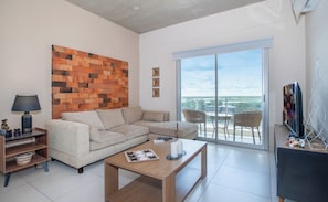 A modern living room with a sectional sofa, a coffee table, a TV, and a large window with a view.