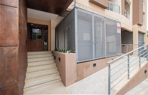 A building entrance with a set of stairs leading to a door, a metal gate with a sign, and a staircase railing.