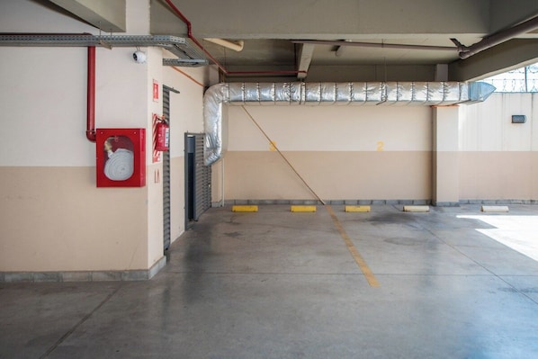 A parking garage with concrete floors, a fire extinguisher, and a ventilation duct.