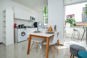 Cozinha moderna com armários brancos, máquina de lavar e área de jantar com mesa e cadeiras.