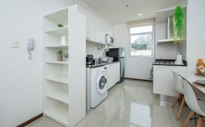 Cozinha compacta com máquina de lavar, micro-ondas e área de refeições com mesa e cadeiras.