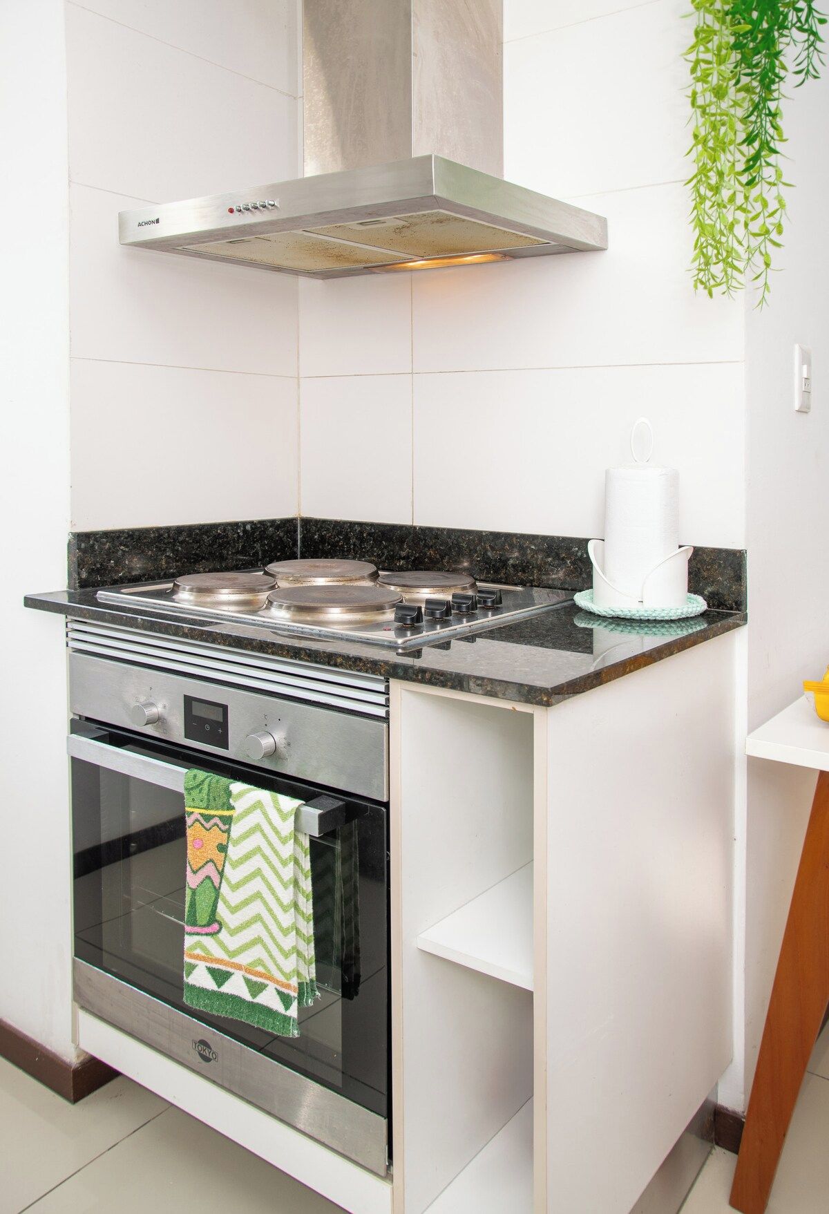 Cozinha compacta com forno embutido, exaustor de aço inoxidável e bancada pequena.