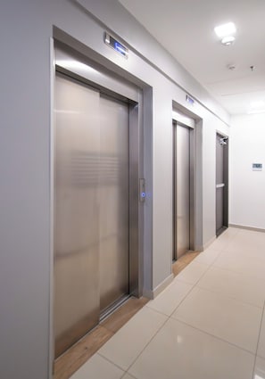 Corredor com três portas de elevador, cada uma com visor digital e painel de controle.