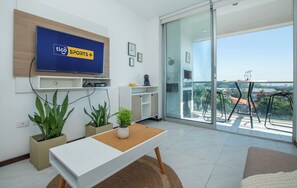 Sala de estar moderna com televisão de tela plana, varanda com mesa e cadeiras, e plantas em vasos.