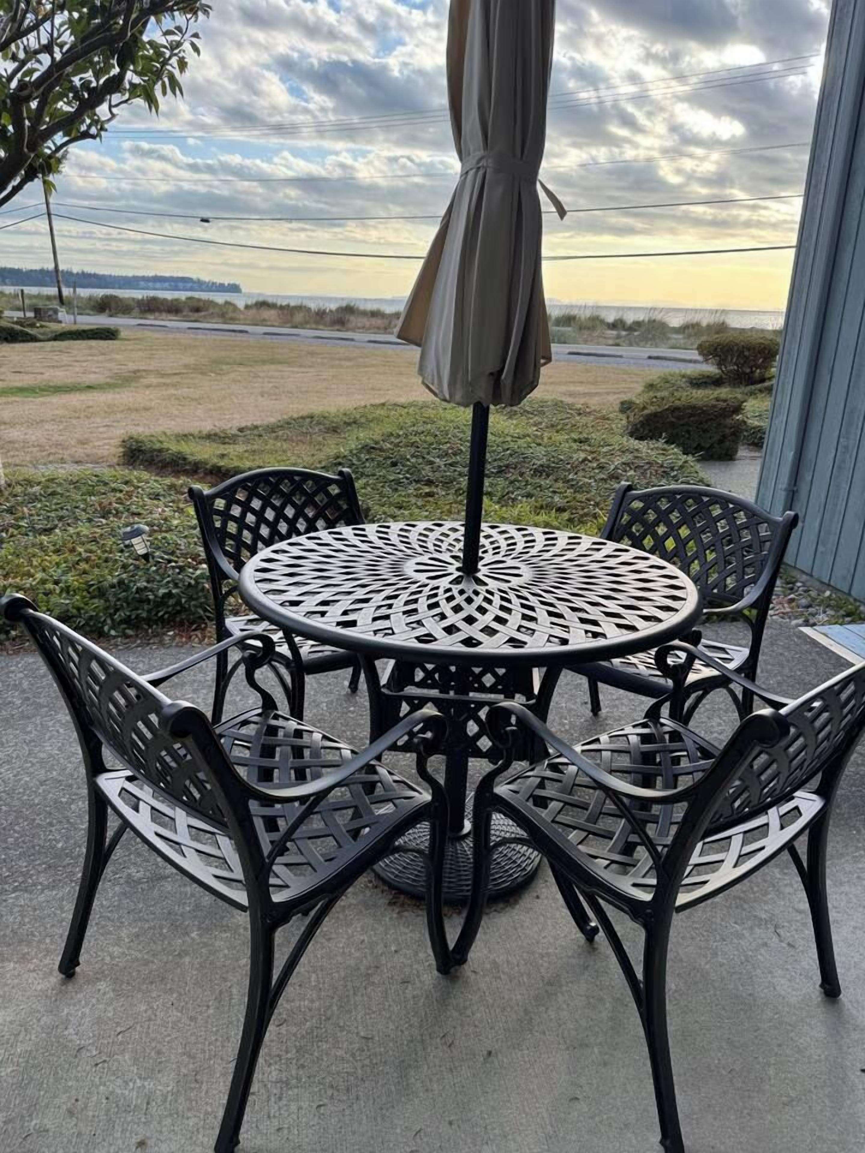 An outdoor patio with a round metal table and chairs, an umbrella, and a view of the ocean.