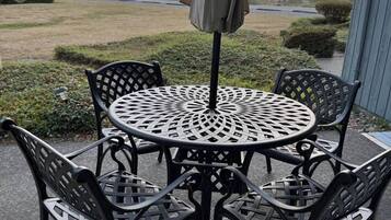 An outdoor patio with a round metal table and chairs, an umbrella, and a view of the ocean.