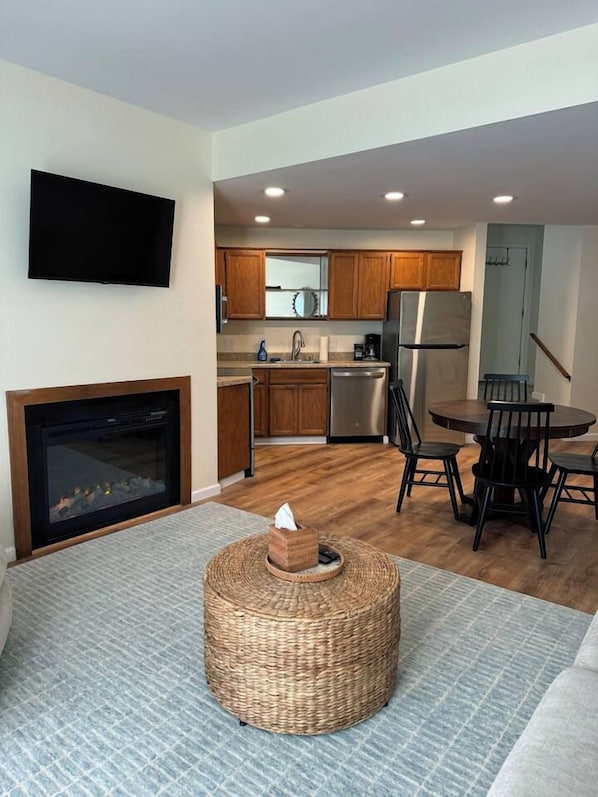 A modern kitchen with wooden cabinets, a stainless steel refrigerator, and a dining area with a round table and chairs. - Sunset Shores | Beach View Condo w/ Patio (Blaine)