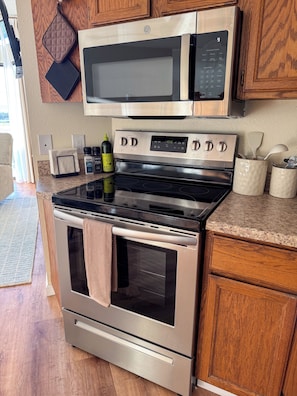 A kitchen with a stainless steel refrigerator, microwave, and oven, wooden cabinets, and a granite countertop. - Sunset Shores | Beach View Condo w/ Patio (Blaine)