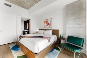 Un dormitorio moderno con una cama de madera, un banco verde, una mesita de noche y un cuadro abstracto colgado en la pared.