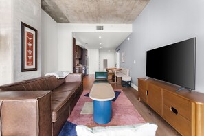 Una sala moderna con un sofá de cuero marrón, una mesa de centro azul, un mueble de televisión de madera y un televisor de pantalla plana grande.