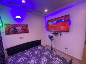 A bedroom with a bed, a wall-mounted TV, and a painting.