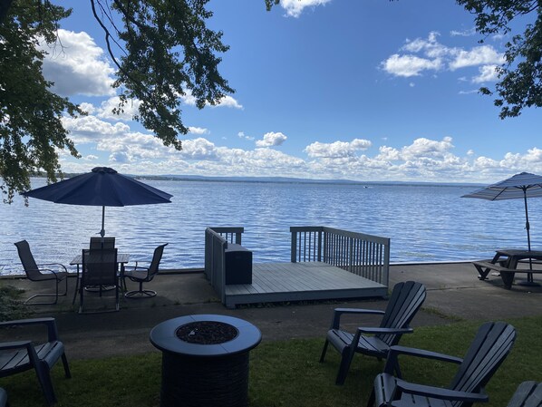 An outdoor seating area with chairs, a table, and an umbrella, overlooking a calm body of water.