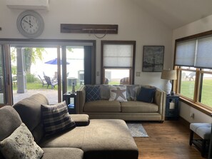 A living room with a sofa, a clock, and a view of the outdoors.