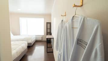 Habitación de hotel con dos camas, una mesita pequeña y un toallero de pared con toallas blancas.