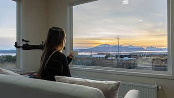 Una habitación con un ventanal grande, un sofá y una persona sosteniendo una taza.