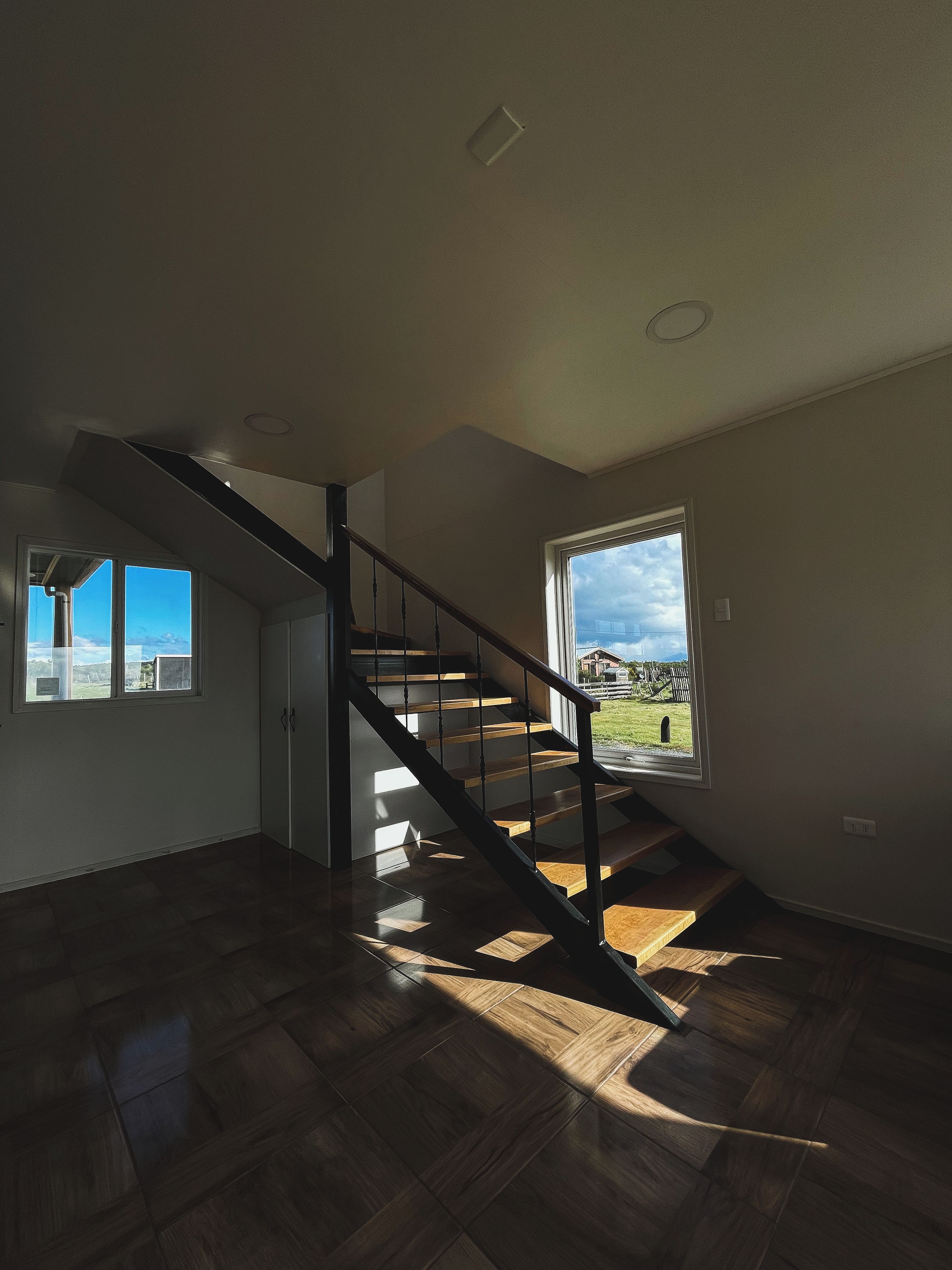 Un interior moderno con una escalera de madera, un ventanal y vistas al exterior.