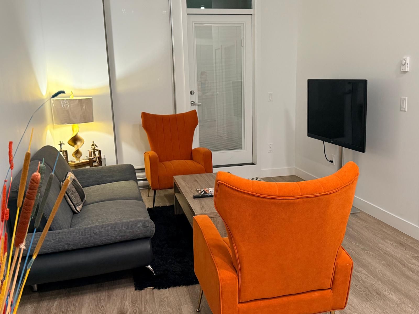 Ein modernes Wohnzimmer mit einer Couch, zwei Sesseln, einem Couchtisch, einem Fernseher und einer Lampe.