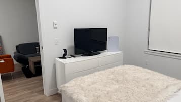A bedroom with a bed, a television, a white dresser, a chair, and a small table.