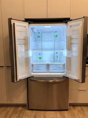 Ein offener Kühlschrank mit übersichtlichen Aufbewahrungsbehältern und Wasserflaschen im Inneren.