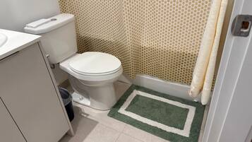 A bathroom with a toilet, a bidet, a shower curtain, and a small rug.