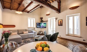 Ein Wohnzimmer mit einer Couch, einem Esstisch mit Früchten, einem Fernseher und einem Kamin.