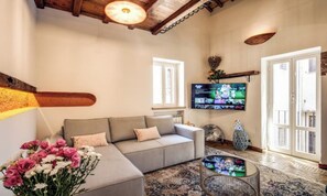 Una sala de estar con un sofá gris, un televisor de pantalla plana, un jarrón decorativo y un ventanal grande.