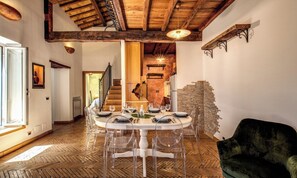 Un comedor con una mesa redonda dispuesta para cuatro, suelo de madera y una escalera que conduce a un nivel superior.