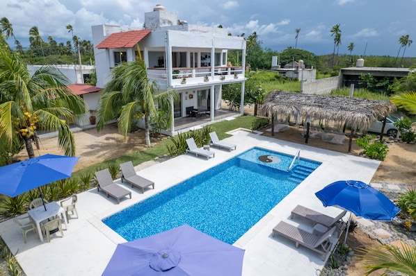 A two-story building with a swimming pool, lounge chairs, and umbrellas.