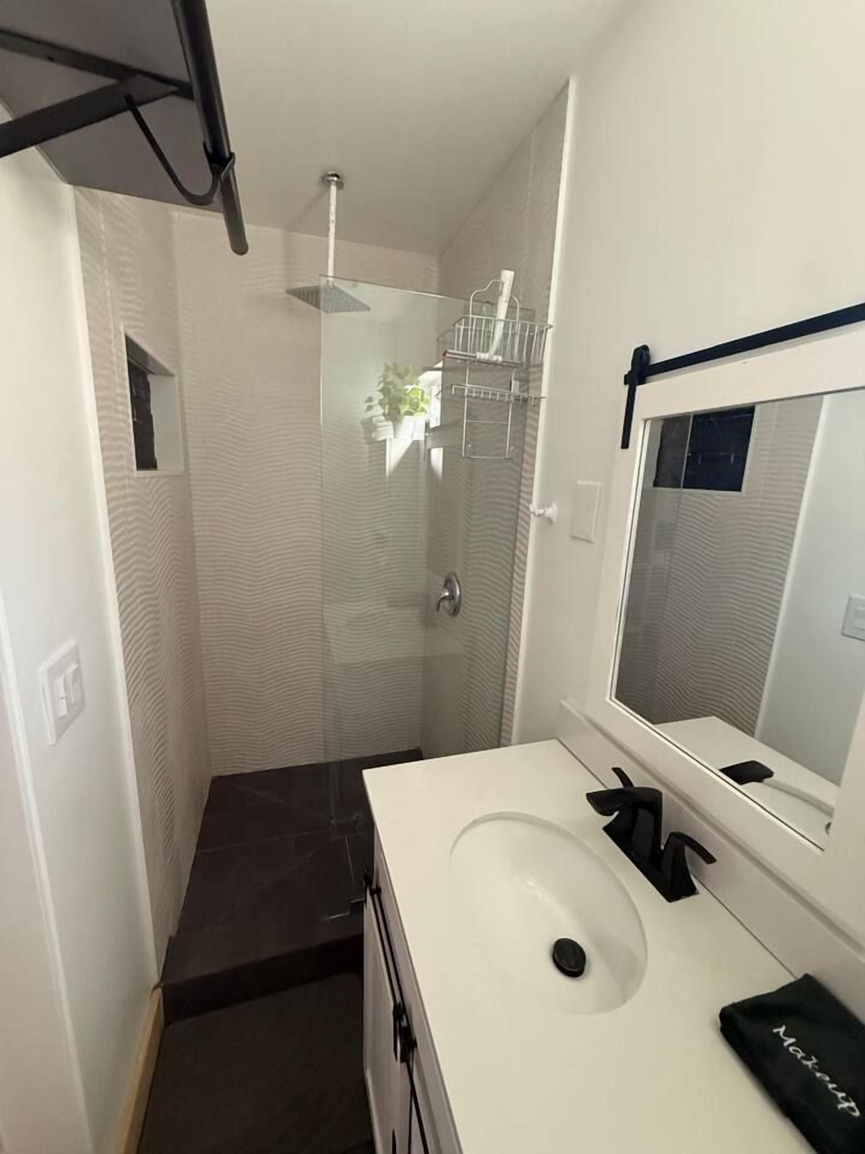 Une salle de bain avec un lavabo blanc, un miroir et un espace douche.