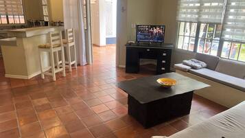 Una sala de estar con un sofá, una mesa de centro, un televisor y una zona de cocina con mostrador y sillas.