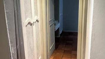Un couloir étroit, dont le sol est recouvert de carreaux, mène à une pièce dotée d’une porte.