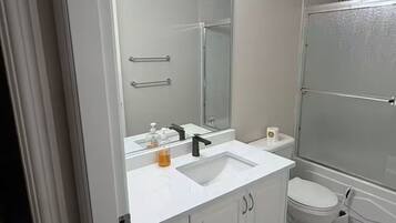 Une salle de bain avec un lavabo blanc, un miroir et un meuble-lavabo, des toilettes et une douche à parois de verre.