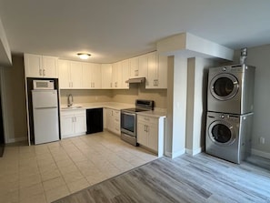 A modern kitchen with white cabinets, a built-in microwave, oven, dishwasher, and a stainless steel washing machine. - Brand new guest suite in Burnaby (Burnaby)